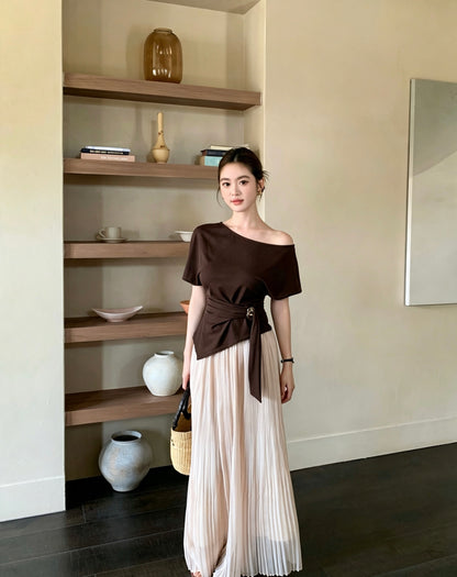 Model posing in an apricot pleated maxi skirt near wooden shelves