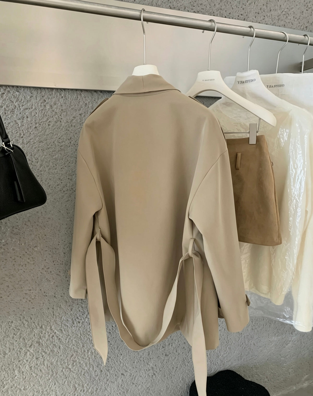 Back view of a beige trench coat hanging on a rack showing tie waist