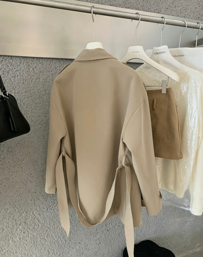 Back view of a beige trench coat hanging on a rack showing tie waist