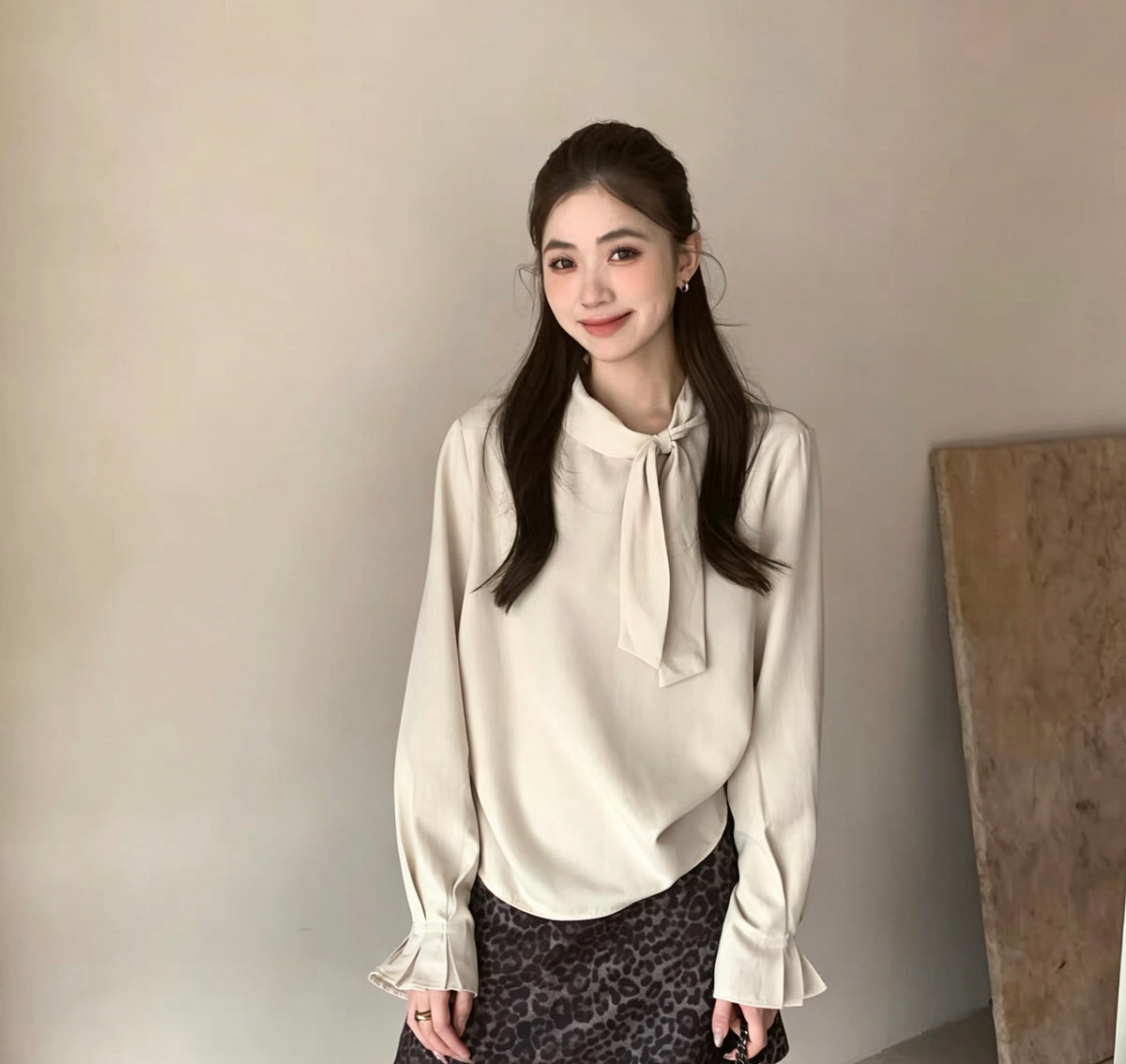 Model wearing apricot tie-neck long-sleeve shirt close up